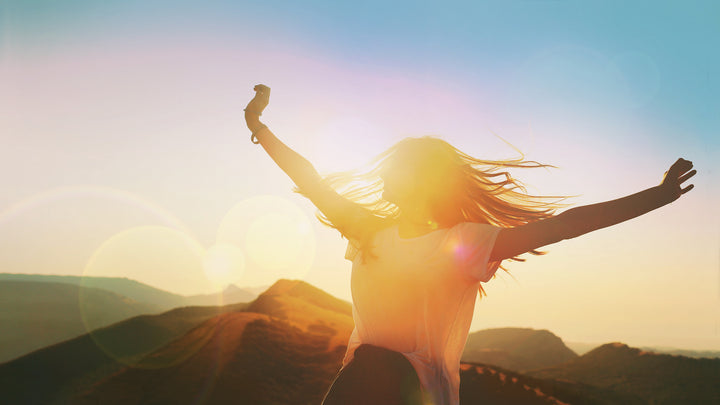 woman with outstretched arms in front of the sunset