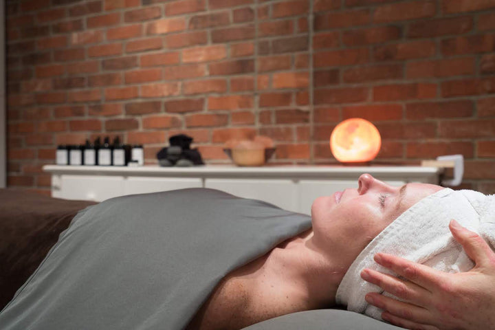 woman getting a facial in pure beauty & wellness spa with himalayan salt lamp and brick wall
