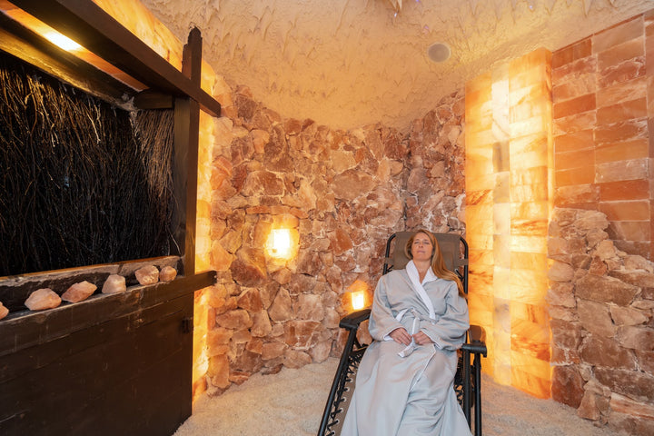 Woman sitting in salt cave in robe with eyes closed.