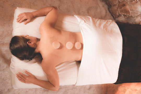 woman laying on a massage table with pink salt stones on her back with white sheet and blank blanket in a salt cave